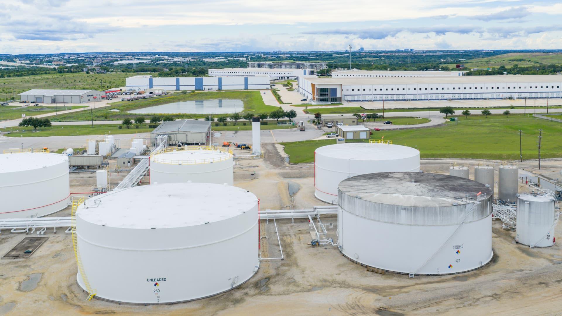 An aerial drone view of large white fuel storage tanks at an energy terminal under a cloudy sky, illustrating the June 24 2026 ThriveInMarkets evening review oil section as WTI crude fell about 4 percent toward 70 dollars and briefly traded below it, the first dip under 72 dollars since early March, after a US-Iran interim agreement reopened the Strait of Hormuz and tankers resumed transit, easing fears of a prolonged Middle East supply disruption