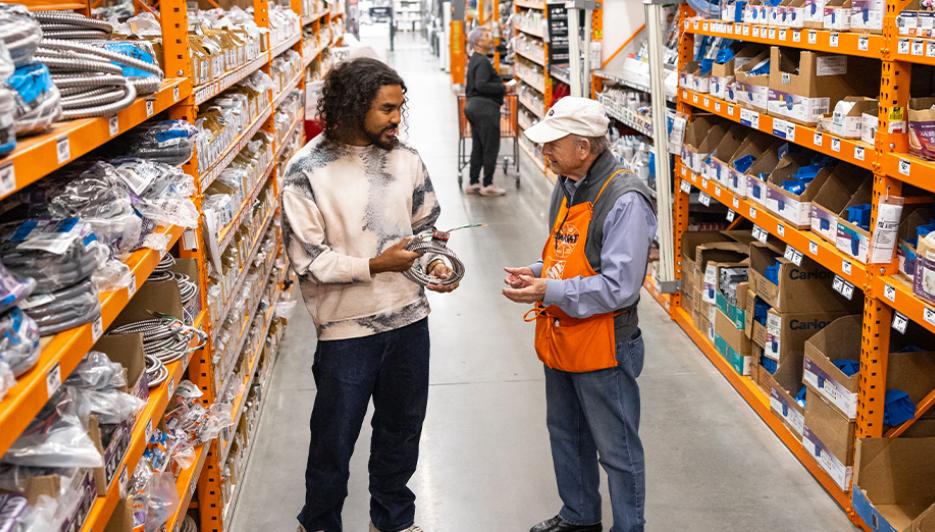 A Home Depot associate in an orange apron helps a customer choose plumbing parts in a store aisle on Tuesday August 18 2026, the session Home Depot beat second-quarter sales at 47.9 billion dollars and reaffirmed guidance even as July US housing starts crashed 12.4 percent to a 1.239 million annual rate