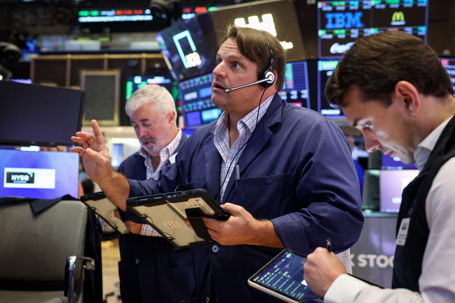 NYSE floor traders in blue jackets work tablets and screens on Tuesday August 25 2026, the session the S&P 500 closed at 7,677.28 up 0.32 percent as technology recovered into Nvidia's Wednesday print, West Texas Intermediate dropped about 5 percent to near 80.70 dollars after Monday's Bessent Iran-sanctions briefing, and Dick's Sporting Goods posted its worst session on record, down 30.68 percent to 124.31 dollars after missing second-quarter results and cutting full-year guidance