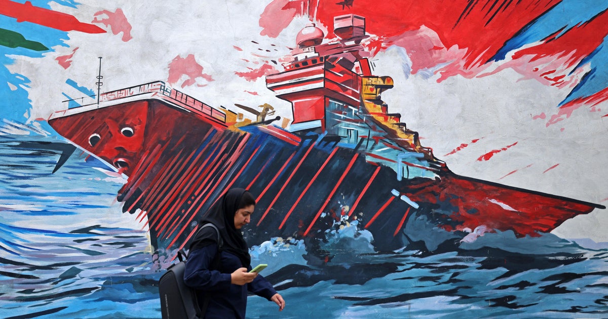 A woman walks past a Tehran mural of a warship in red, white and blue, used as the ThriveInMarkets evening-review inline image for Monday August 31 2026, when West Texas Intermediate held near 85.60 dollars after Sunday US strikes on Iranian launchers at Larak Island that Central Command said were preparing to fire sea mines into the Strait of Hormuz