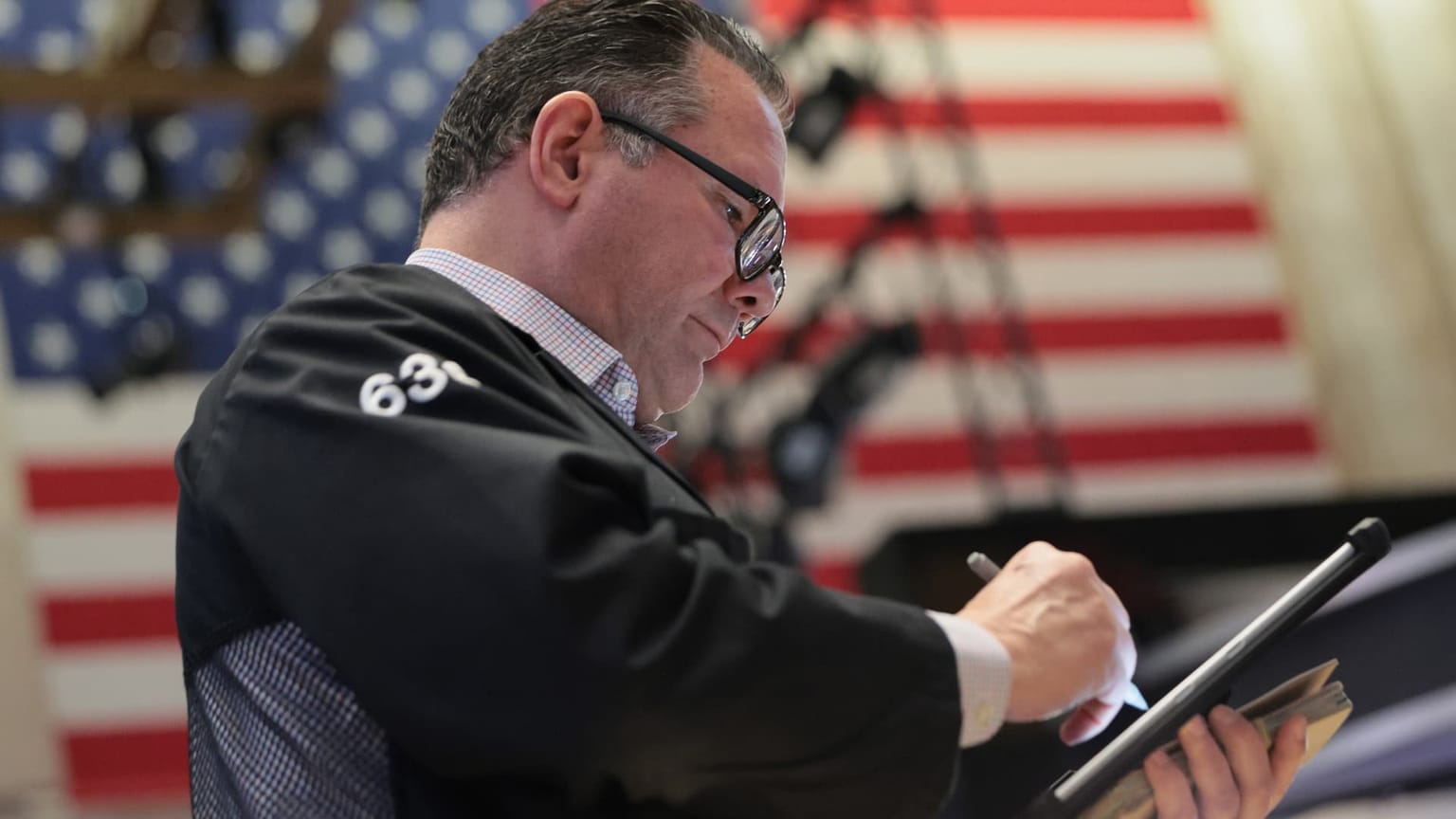 A New York Stock Exchange floor trader in a black jacket numbered 63 writes on a tablet in front of an American flag, used as the ThriveInMarkets evening-review hero for Thursday September 10 2026, when the S&P 500 closed 7,591.70 after breaking Wednesday's 7,624.16 cash low, West Texas Intermediate settled 102.48 dollars, and the 10-year Treasury yield jumped to about 4.96 percent as August PPI and a 6 percent oil surge lifted September Fed hike odds toward 70 percent