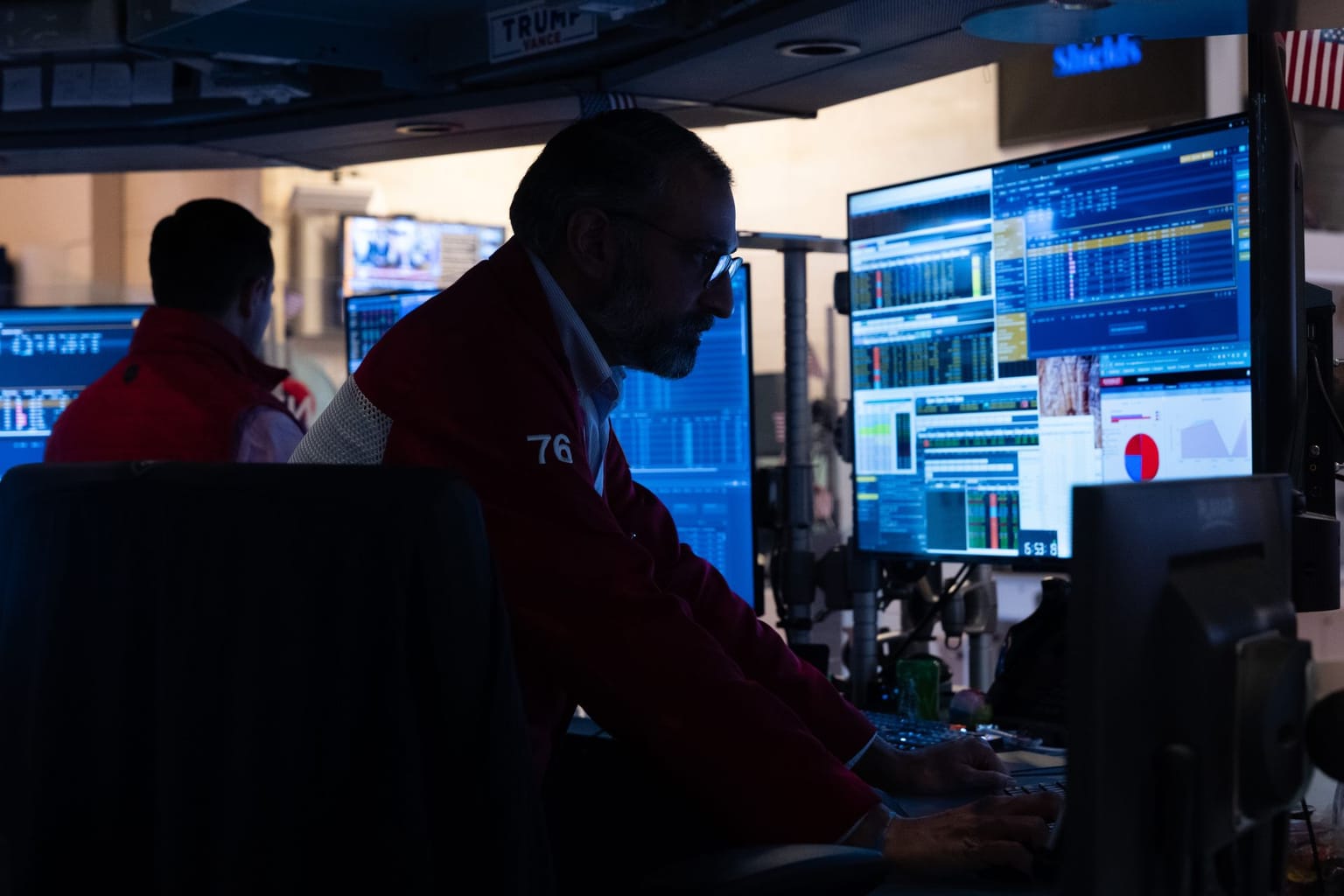 A New York Stock Exchange floor trader numbered 76 works a bank of blue quote screens in a red jacket, used as the ThriveInMarkets evening-review hero for Monday September 14 2026, when the S&P 500 closed 7,619.98, chip stocks sold off after AI chiefs called for a development slowdown, CrowdStrike jumped about 14 percent, and West Texas Intermediate faded to about 101.92 dollars after a 104.95 dollar high