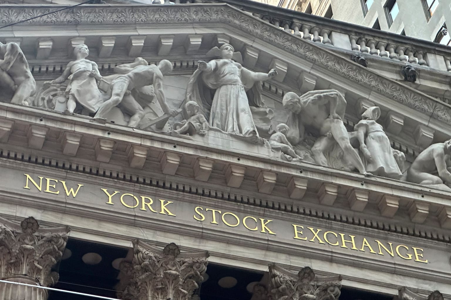 The New York Stock Exchange pediment and gold lettering on the Broad Street facade, used as the ThriveInMarkets evening-review hero for Monday October 5 2026, when the Nasdaq Composite closed 27,477.31 at a record, the S&P 500 closed 7,773.95 up 0.7 percent, and Nvidia closed 238.90 dollars at a record