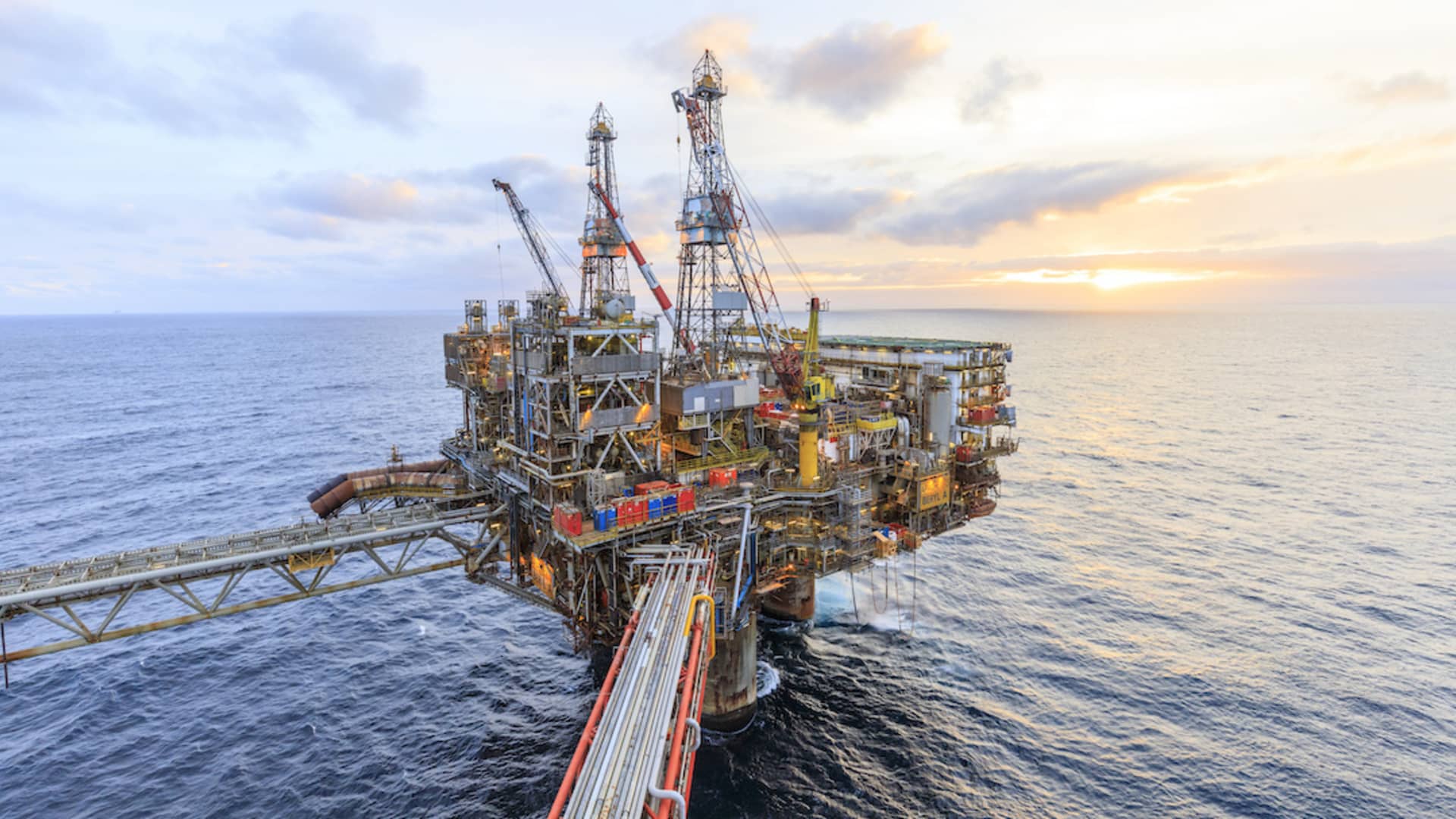 An offshore oil production platform with twin drilling derricks and crane towers stands on a calm sea at sunset under a glowing amber sky, illustrating the June 12 2026 ThriveInMarkets morning analysis as WTI front-month crude fell roughly 4.5 percent to about 83.80 dollars a barrel, its lowest level in nearly two months, after Iranian state media reported a proposed United States and Iran peace deal that would reopen the Strait of Hormuz within 30 days and President Trump said documents could be signed over the next few days, even as Tehran's Fars outlet pushed back that no draft text had been approved, while Brent crude slipped about 4.4 percent to around 86.45 dollars, the S&P 500 closed June 11 up 1.75 percent at 7,394.30 with E-mini futures pointing higher near 7,428 ahead of the record 1.75 trillion dollar SpaceX initial public offering debut on the Nasdaq under ticker SPCX, spot gold eased below 4,200 dollars near 4,210, Bitcoin firmed about 2 percent to around 63,600 dollars and Ethereum lagged near 1,674 dollars