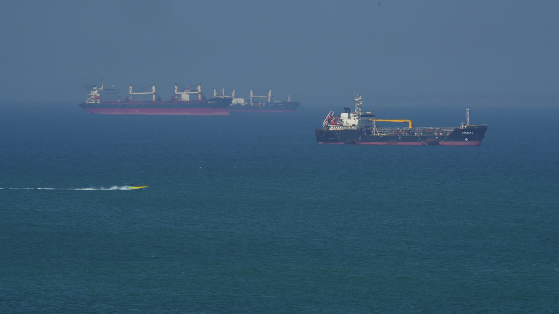 Oil tankers and a cargo ship sit at anchor on calm blue water near the Strait of Hormuz under a hazy sky, illustrating the June 15 2026 ThriveInMarkets morning analysis as a US-Iran peace deal set to reopen the strait sent WTI crude tumbling about 5 percent to 80.49 dollars, while Bitcoin rose to 65,627 dollars, Ethereum to 1,716 dollars, gold firmed to 4,219 dollars and the S&P 500 held near its 7,431 record ahead of Kevin Warsh's first FOMC meeting and dot plot on Wednesday June 17