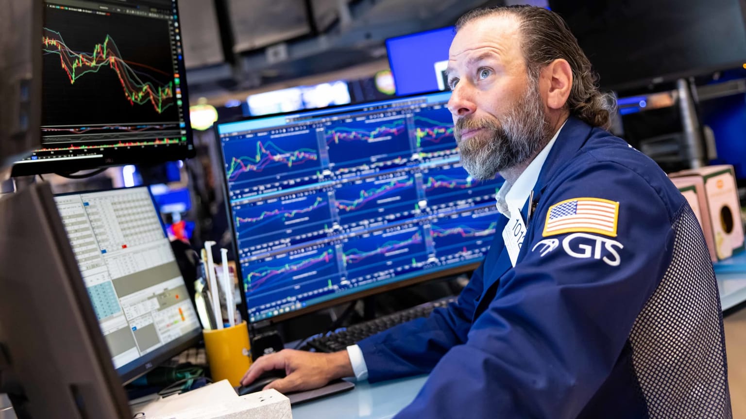 A New York Stock Exchange floor trader in a navy jacket watching multiple monitors filled with price charts, illustrating the ThriveInMarkets morning analysis for Monday July 6 2026 as US cash equity trading resumes after the July 4 Independence Day holiday with S&P 500 futures pointing back toward record highs, SpaceX preparing to join the Nasdaq-100, a delayed June ISM Services PMI due today and the first FOMC minutes of the Kevin Warsh era arriving Wednesday July 8.