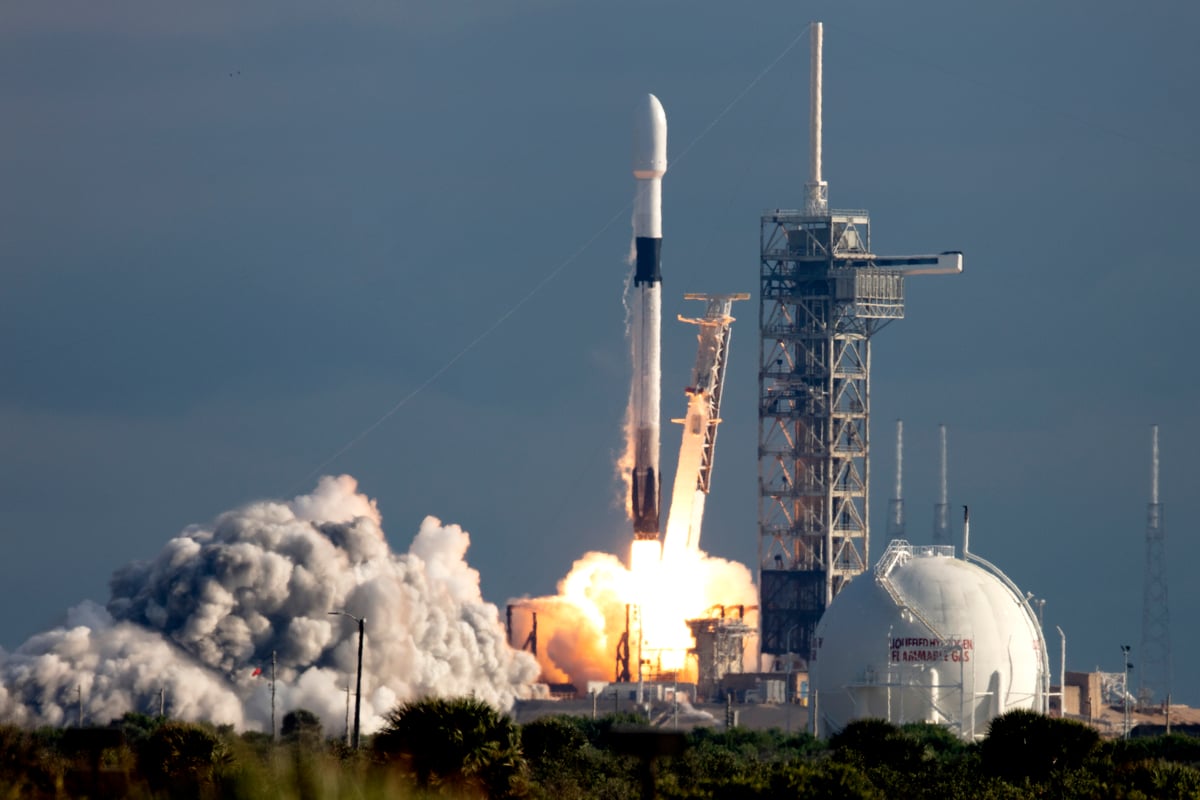 A SpaceX Falcon 9 rocket lifting off in a plume of fire and smoke from its launch pad against a blue sky, illustrating the ThriveInMarkets morning analysis for Tuesday July 7 2026 as SpaceX officially joins the Nasdaq-100 before the opening bell in a fast-tracked inclusion that JPMorgan estimates could force roughly 4.3 billion dollars of passive buying from index trackers such as the Invesco QQQ and QQQM, with S&P 500 E-mini futures near 7,593 pointing toward another record after Monday's all-time closing high of 7,537.43 and the Dow Jones Industrial Average's first close above 53,000, memory and semiconductor stocks still leading after Nvidia supplier Hon Hai reported strong quarterly sales, Bitcoin holding near 63,083 dollars while Ethereum eases near 1,772 dollars and US spot Bitcoin ETFs snap a ten-day outflow streak, XRP steadying near 1.14 dollars after Ripple won a Luxembourg MiCA licence, gold near 4,131 dollars and WTI crude near 69.10 dollars ahead of Wednesday's first FOMC minutes of the Kevin Warsh era