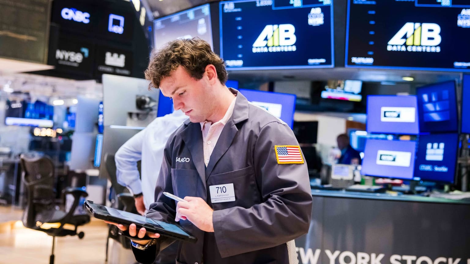 A trader works on the floor of the New York Stock Exchange surrounded by glowing market data screens, used in the ThriveInMarkets morning analysis for Wednesday July 15 2026 after a cooler-than-expected June CPI print knocked Federal Reserve rate-hike odds below 20 percent and lifted the S&P 500 back toward its record near 7,543, big banks led by Goldman Sachs beat earnings, IBM slumped 22 percent, Ether jumped about 6 percent to $1,868, gold held near $4,023 and WTI crude stayed above $80 on Strait of Hormuz supply risk