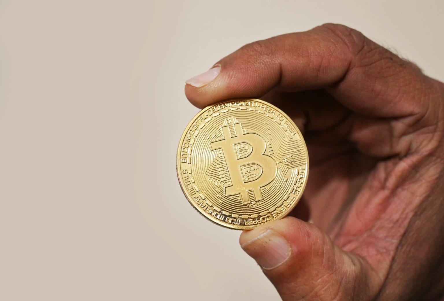A physical golden Bitcoin token held up in a hand, symbolising the crypto news on Thursday August 13 2026 when Bitcoin steadied near 63,800 dollars after a tame US inflation print, Goldman Sachs agreed to buy exchange traded fund manager NEOS for 2.25 billion dollars to pick up a roughly one billion dollar Bitcoin covered call fund, and Fidelity asked the Securities and Exchange Commission for approval to let its Ethereum fund stake up to 100 percent of its holdings and pay quarterly cash rewards while Ether traded near 1,896 dollars