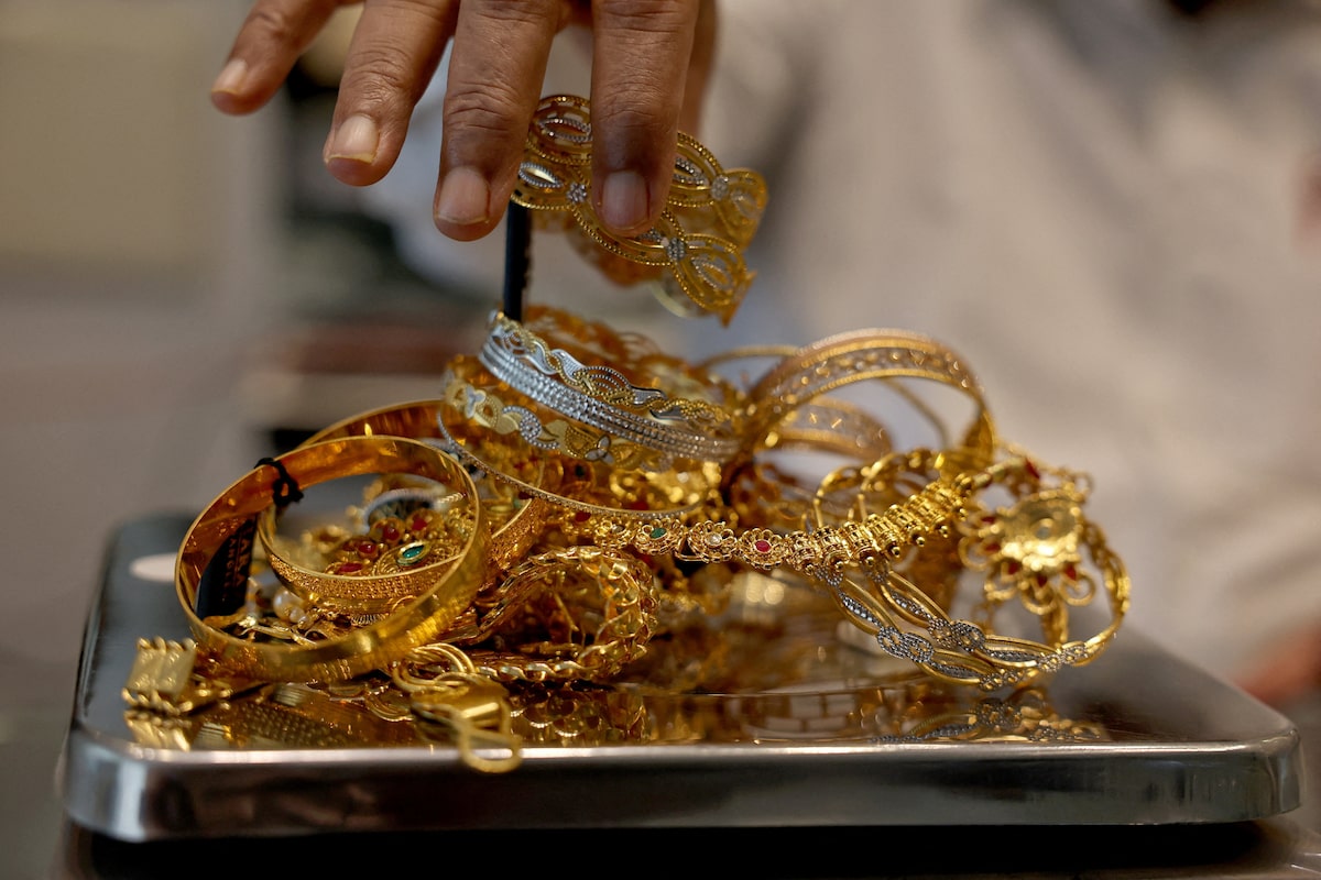 A goldsmith's hand lifts ornate gold and two-tone bangles from a metal weighing tray in an Ahmedabad showroom, marking Tuesday August 18 2026 when spot gold eased back under 4,400 dollars to about 4,398 after Monday evening's 4,419 print as bond yields climbed and oil held the 85-dollar handle