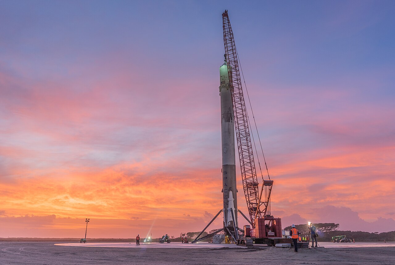 A SpaceX Falcon 9 first stage stands upright after a successful landing at Landing Zone 1, illustrating a June 10 2026 ThriveInMarkets explainer on why SpaceX is going public, as the reusable-rocket economics pioneered by the company underpin a roughly 1.75 trillion dollar valuation while Elon Musk seeks tens of billions of dollars in fresh capital to fund Starship development, a Mars program, and a planned constellation of orbital data centers to support artificial intelligence