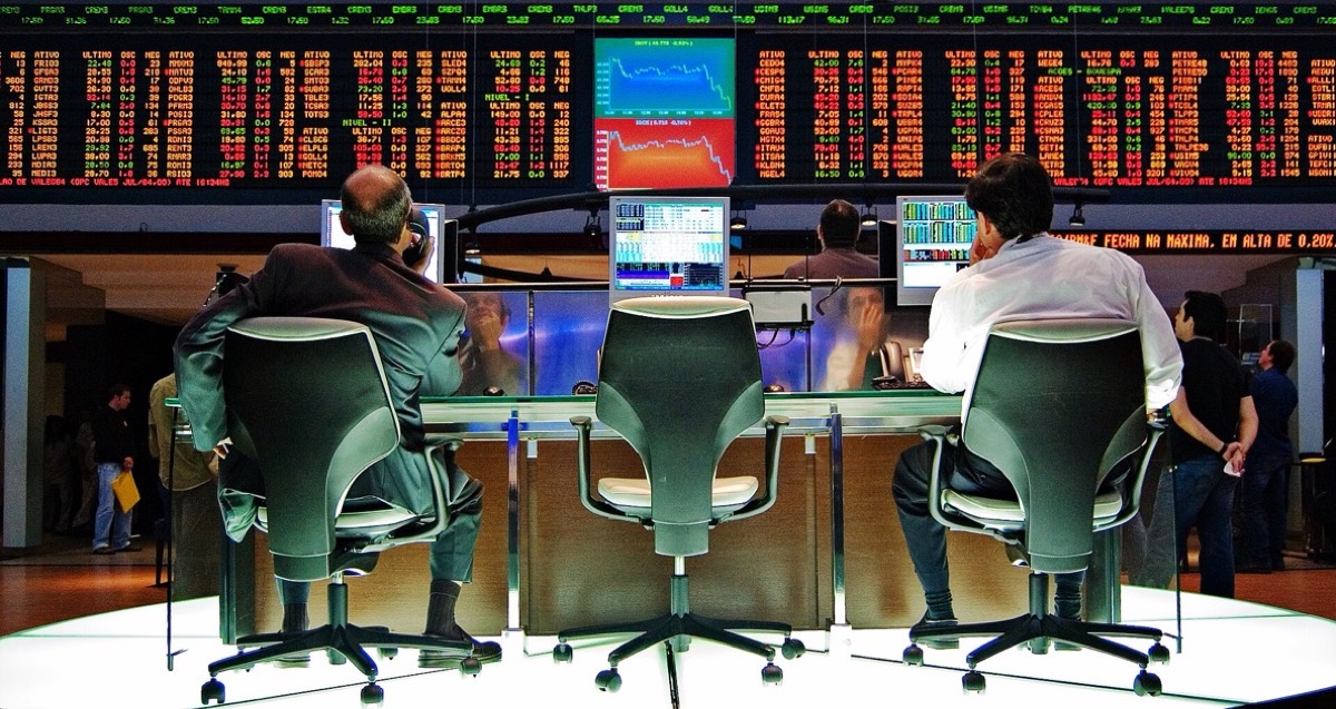 Traders sit at a circular desk under a wall of red and green stock quotes on the B3 exchange floor in Sao Paulo, used as the ThriveInMarkets week-ahead hero for September 14 to 18 2026, when Wednesday's FOMC is 85 to 90 percent priced to hike, Friday's Bank of Japan is widely expected to lift the policy rate to 1.25 percent, and Friday is also quarterly quad-witching