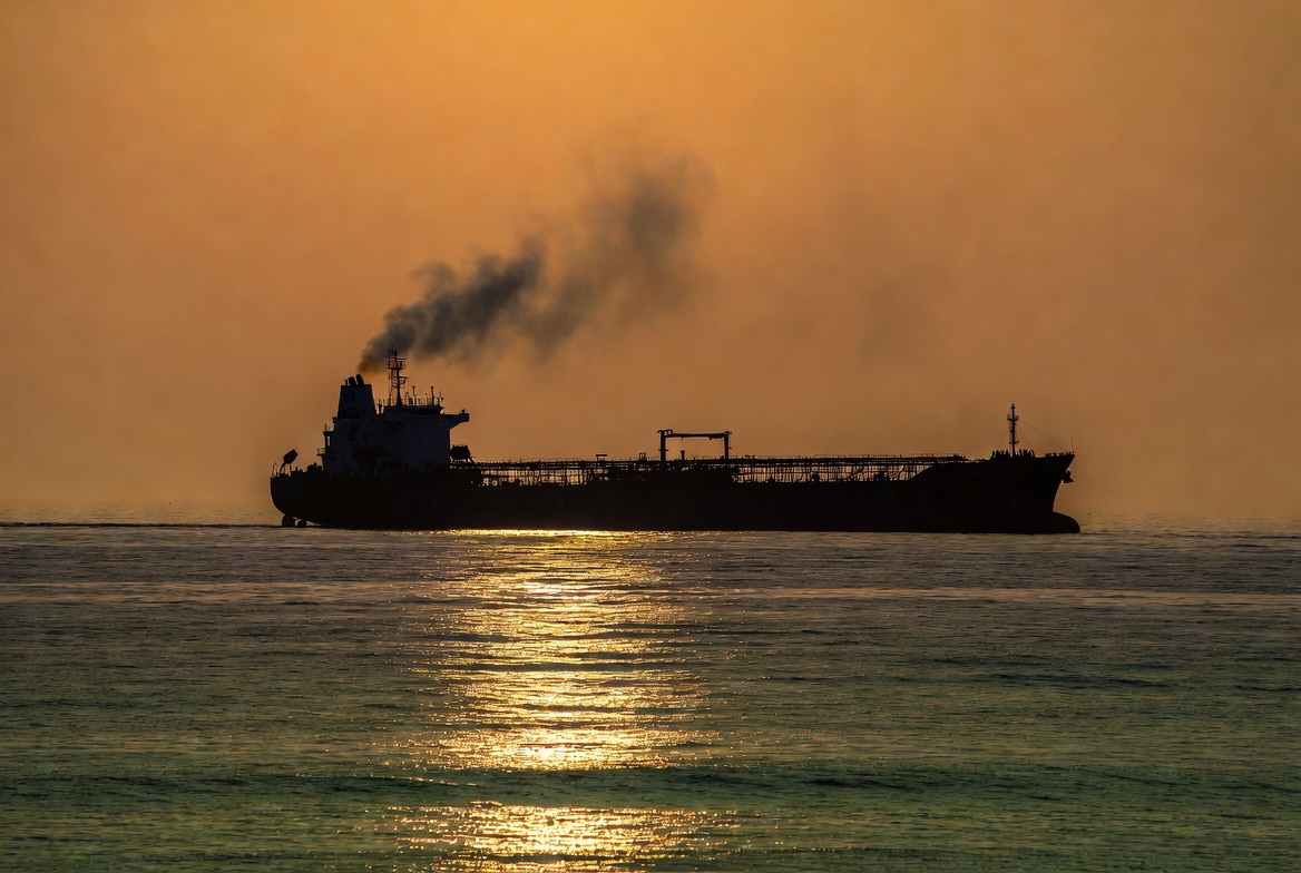 Crude oil tanker silhouetted at sunset with smoke trail rising into a hazy amber sky, representing the WTI 7 percent weekly fade as the 14-point Hormuz Memorandum of Understanding disinflated the war premium and a Friday US-Iran fire exchange briefly lifted crude before the cash session faded the move, WTI settled Friday at $95.48 weekend recap May 10 2026