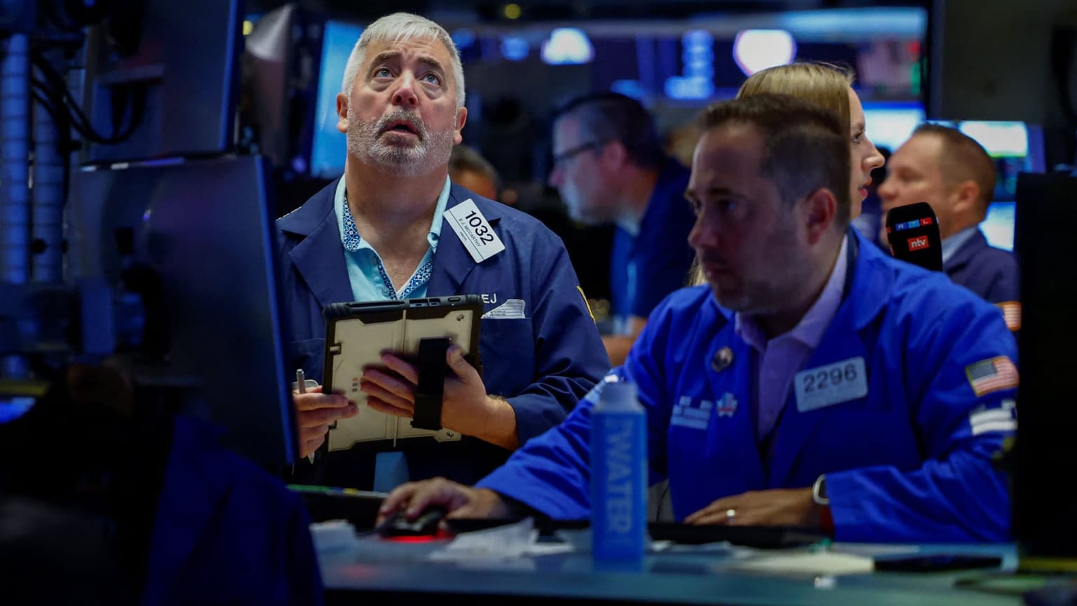 NYSE floor traders in blue jackets work a bank of screens, used as the ThriveInMarkets weekend recap hero for the week of August 17 to 23 2026, when the S&P 500 closed Friday at 7,674.37 down 1.43 percent on the week, snapping a three-week winning streak, while Bitcoin ripped about 22 percent as traditional markets sat closed for the weekend
